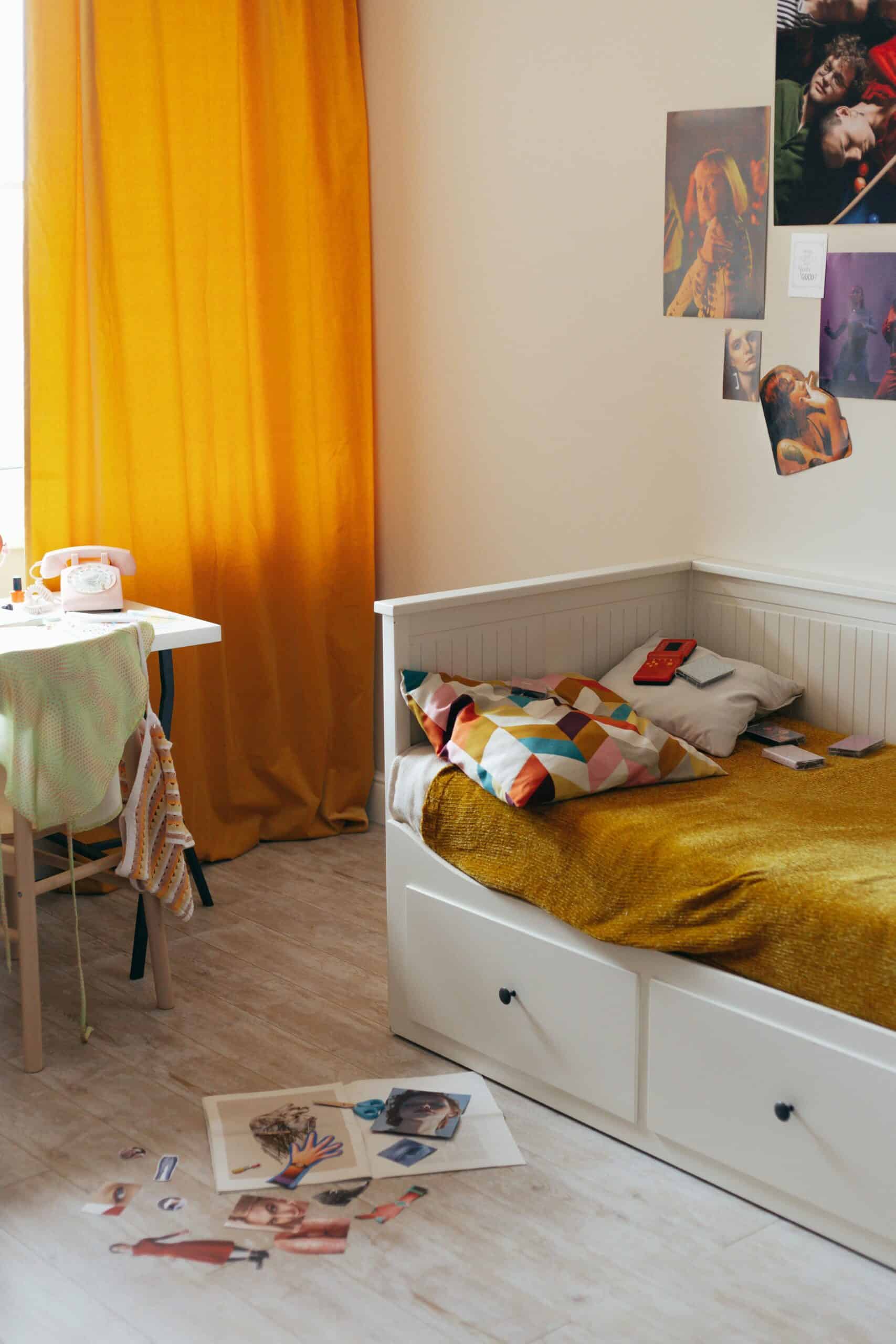 K-pop styled bedroom with mustard yellow curtain, cozy bed, and a small photocard gallery on the wall.