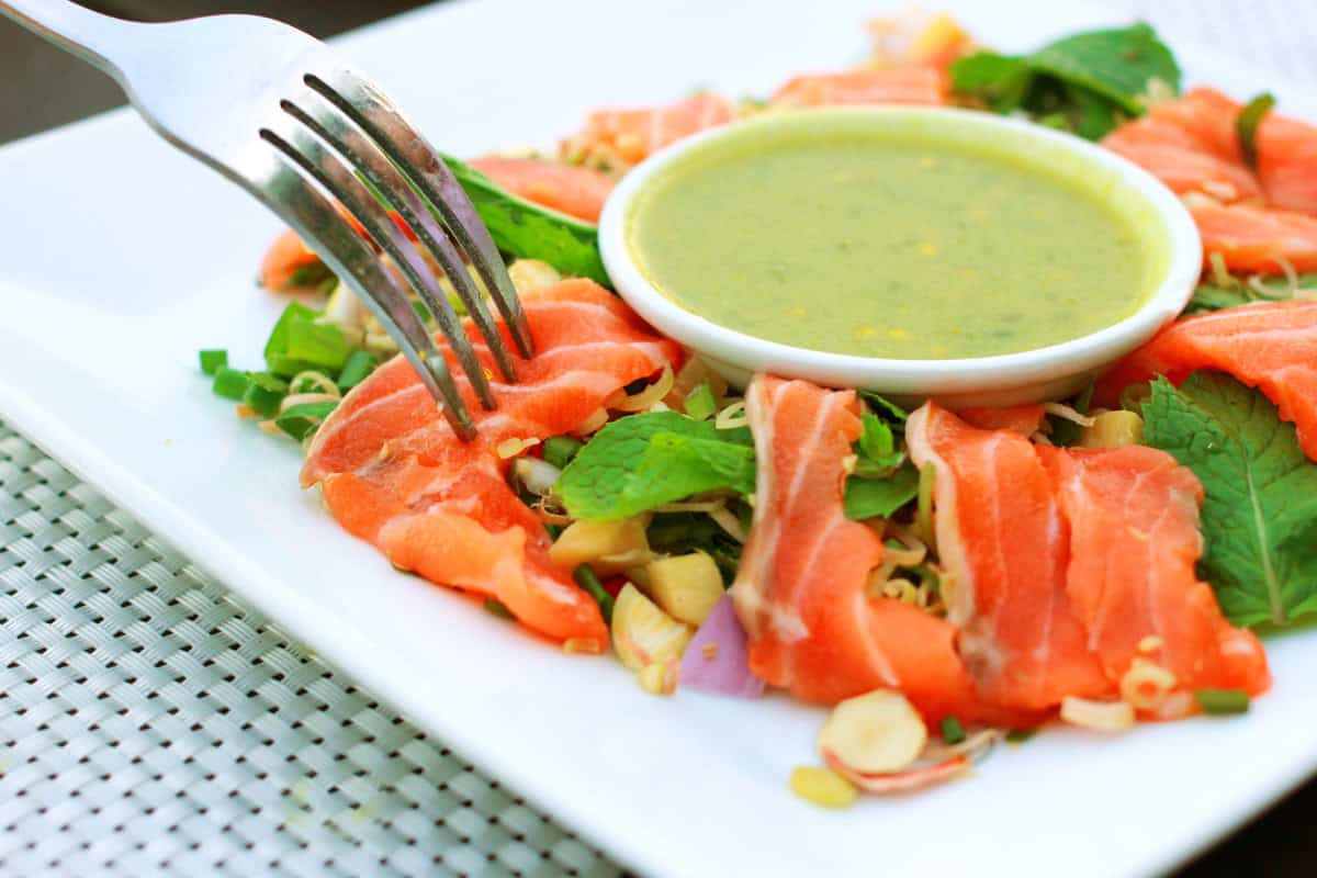 Fresh salmon sashimi with greens and green sauce.