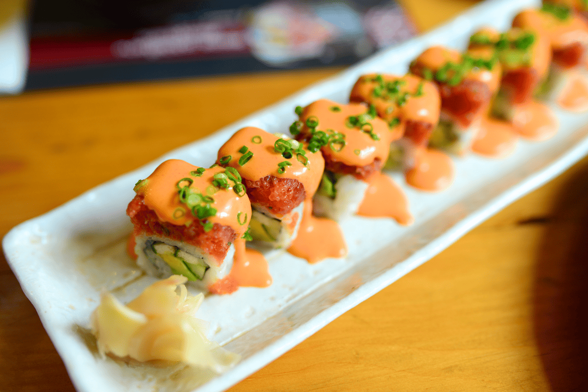 A plate of sushi set, topped with sauce and sliced spring onions.