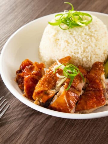 Chicken on a plate of rice and cucumber with peanut sauce.