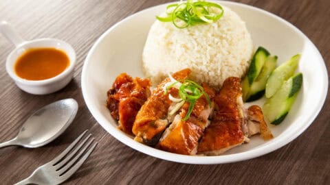 Chicken on a plate of rice and cucumber with peanut sauce.