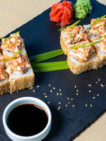 A set of sushi in a plate with different dipping sauces on the side.