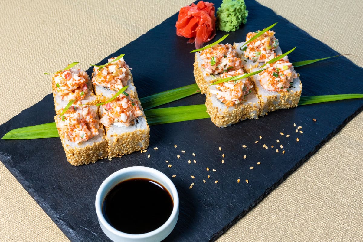 A set of sushi in a plate with different dipping sauces on the side.