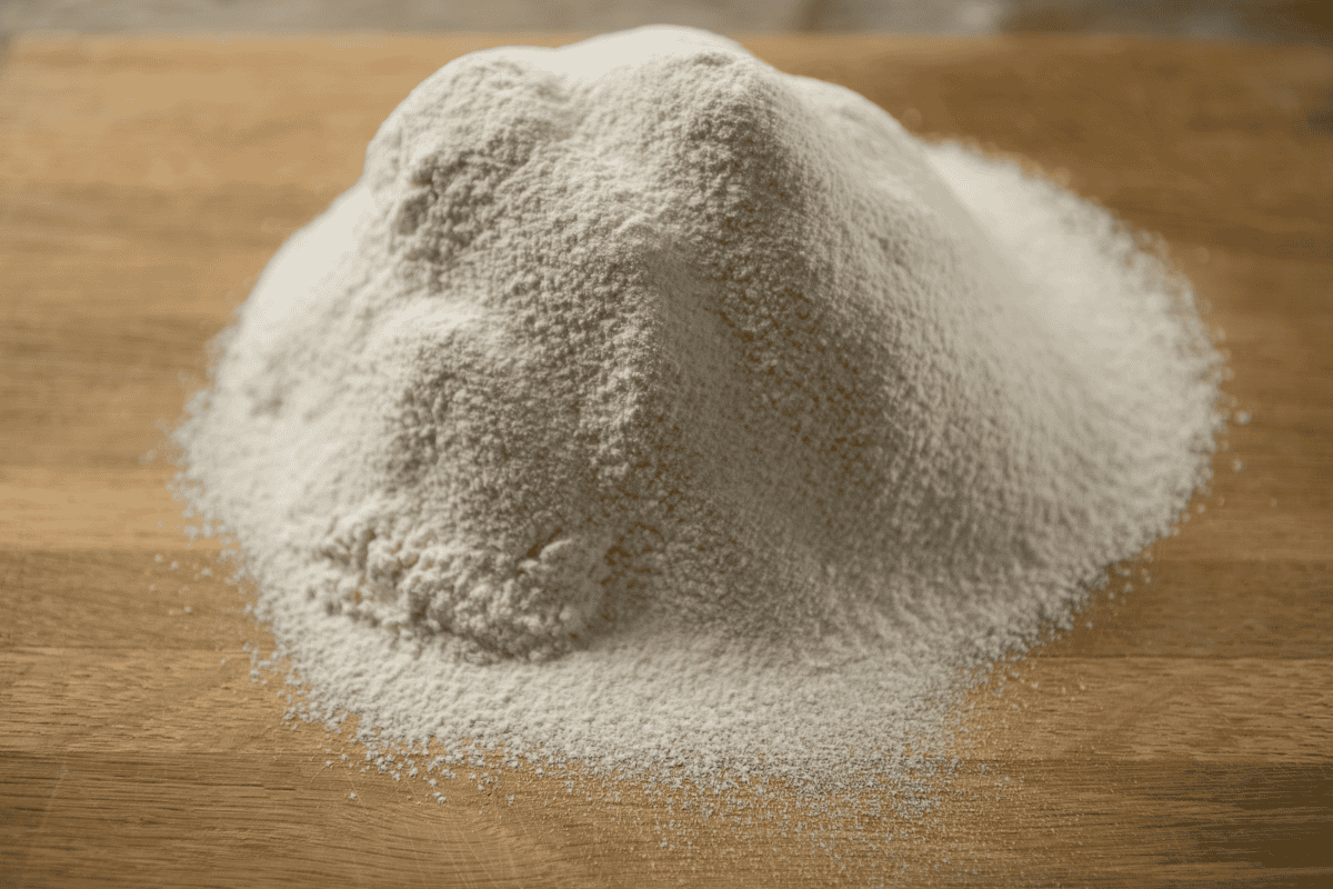 Pile of flour dusted over a wooden flat surface.