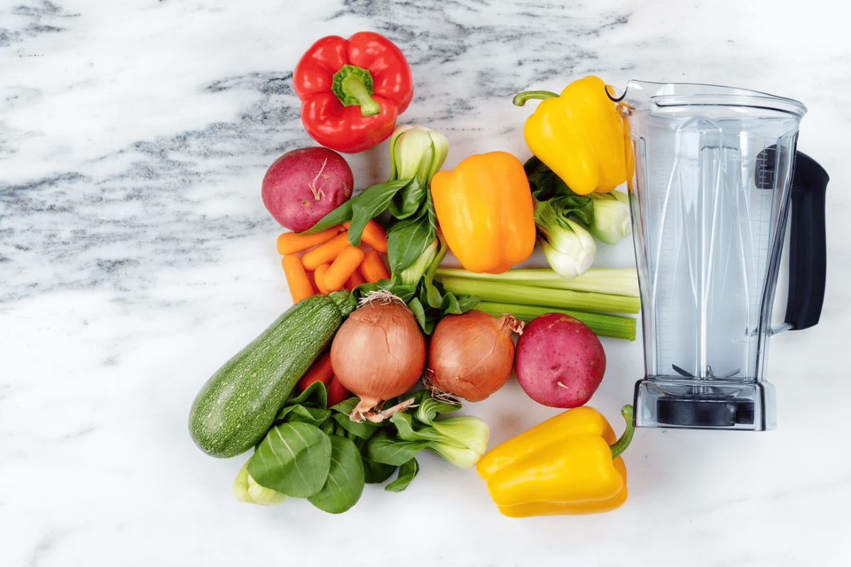 A pile of fresh vegetables next to a blender, ready to be pureed.
