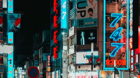 A busy night street in Tokyo filled with neon signs, billboards featuring music groups, and a crowd of pedestrians&mdash;capturing the vibrant energy of a city where pop culture thrives.