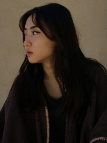 Young woman with dark hair and makeup, looking sideways against a neutral background.