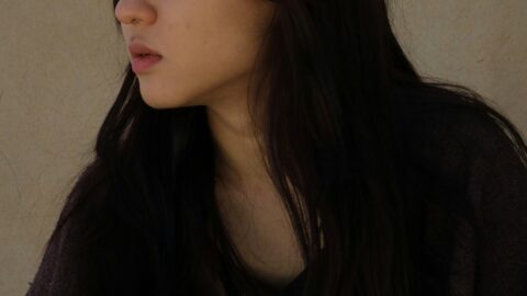Young woman with dark hair and makeup, looking sideways against a neutral background.