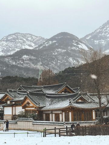 Snow-covered traditional Korean Hanok village with mountain backdrop in Seoul, Korea.