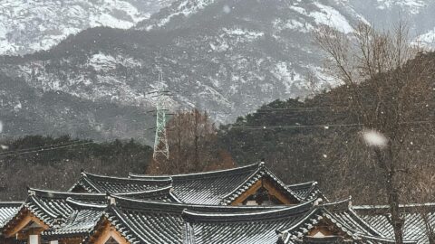 Snow-covered traditional Korean Hanok village with mountain backdrop in Seoul, Korea.