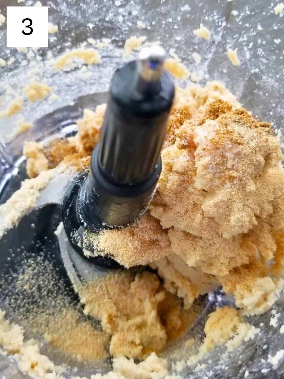 A blended mixture of tahini and lemon juice in a blender, topped with garlic powder, salt, and cumin.