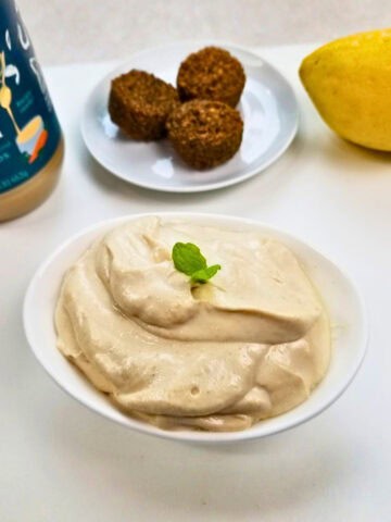 Tahini sauce in a saucer with fresh lemon and a store-bought tahini sauce on the side.