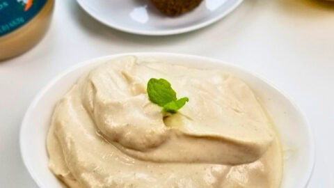 Tahini sauce in a saucer with fresh lemon and a store-bought tahini sauce on the side.
