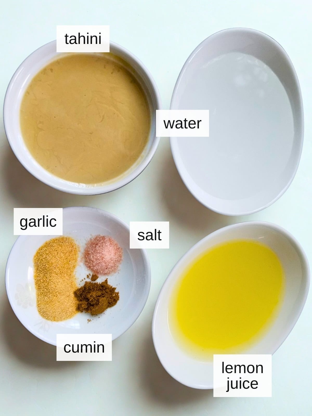 Ingredients for tahini sauce, including water, lemon juice, sea salt, garlic powder, cumin, and tahini.