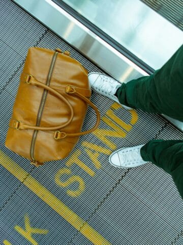 Stylish brown leather duffel bag and white sneakers at Seoul transport hub.