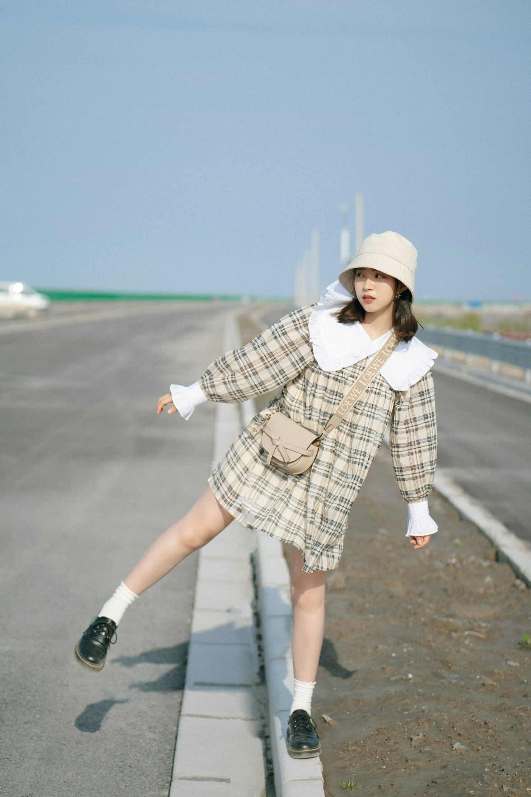 Young woman in stylish plaid outfit on Seoul roadside, posing fashionably near the highway.